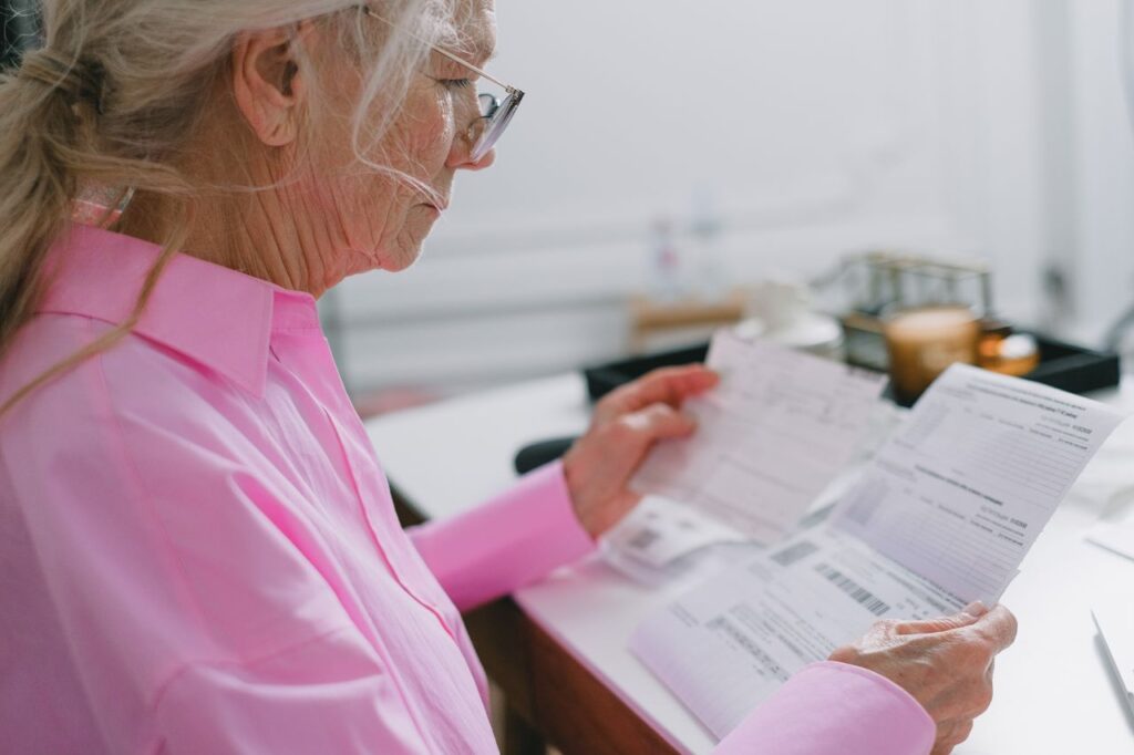 Elderly woman in a pink shirt reviewing paperwork at home.